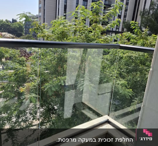 מעקה זכוכית במרפסת עם נוף לעצים ובניינים
